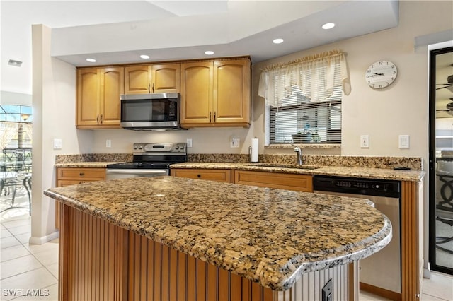 kitchen with a sink, a kitchen island, recessed lighting, appliances with stainless steel finishes, and light stone countertops