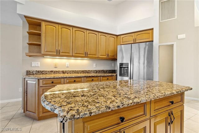 kitchen with light stone countertops, visible vents, open shelves, stainless steel fridge with ice dispenser, and a center island