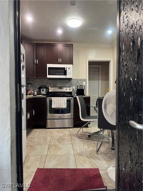 kitchen featuring white microwave, backsplash, ornamental molding, freestanding refrigerator, and electric range