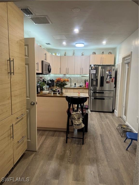 kitchen with a sink, stainless steel appliances, wood finished floors, and decorative backsplash