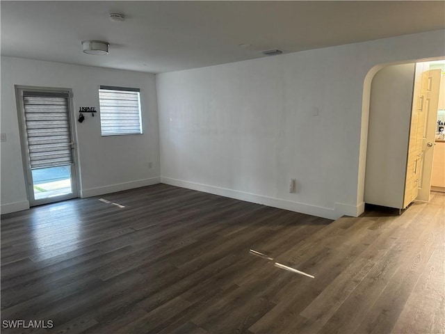 unfurnished room with arched walkways, baseboards, and dark wood-style flooring