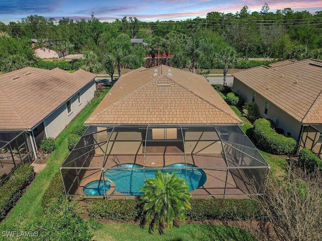 pool at dusk with glass enclosure, a patio, and a pool with connected hot tub