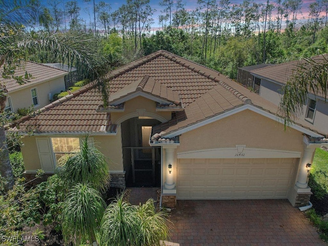 view of front facade with decorative driveway, a tile roof, an attached garage, and stucco siding