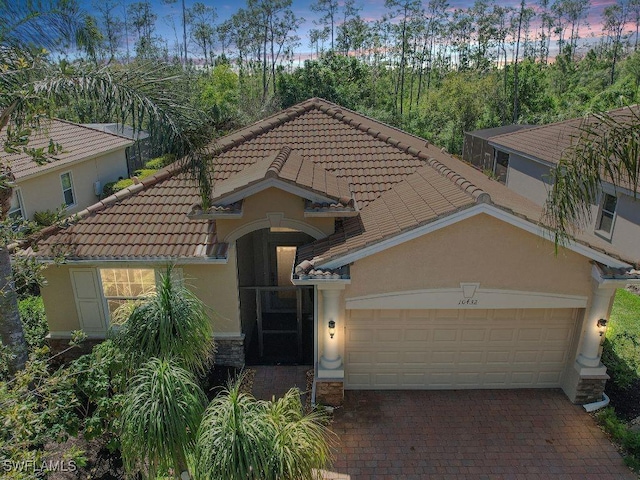 10432 Yorkstone Dr, Bonita Springs, FL 34135 - mediterranean / spanish-style house featuring a tiled roof, stucco siding, a garage, decorative driveway, and stone siding