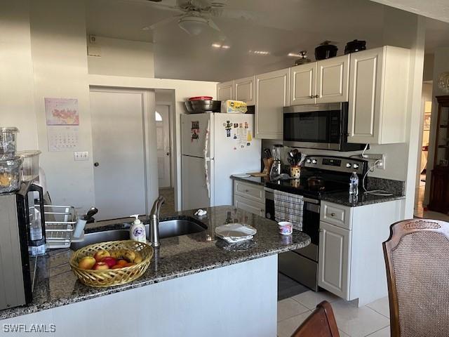 kitchen featuring dark stone countertops, a sink, white cabinetry, appliances with stainless steel finishes, and light tile patterned floors