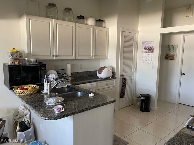 kitchen with a sink, white cabinetry, dark stone counters, a peninsula, and black microwave