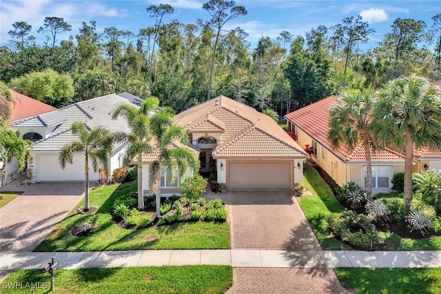 mediterranean / spanish-style house featuring stucco siding, an attached garage, a tile roof, and decorative driveway