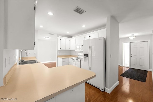 kitchen with a sink, light countertops, a peninsula, white appliances, and dark wood-style flooring