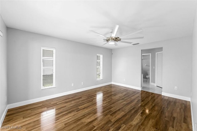 unfurnished room with dark wood finished floors, a ceiling fan, visible vents, and baseboards