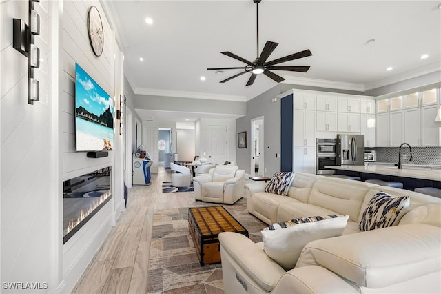 living area with a ceiling fan, a fireplace, recessed lighting, light wood-style floors, and crown molding