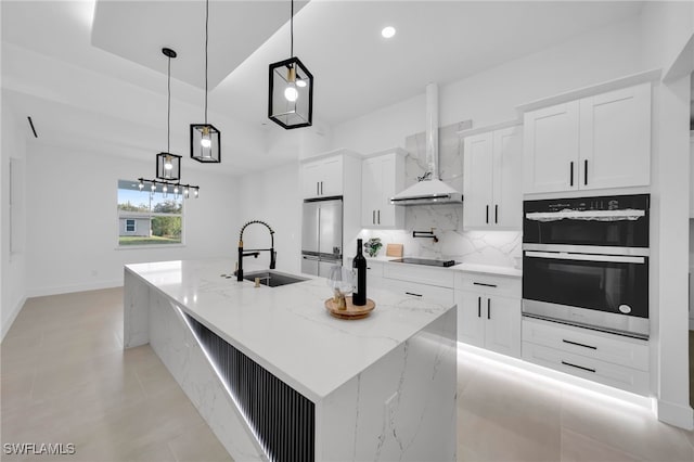 kitchen with tasteful backsplash, appliances with stainless steel finishes, white cabinetry, wall chimney exhaust hood, and a sink