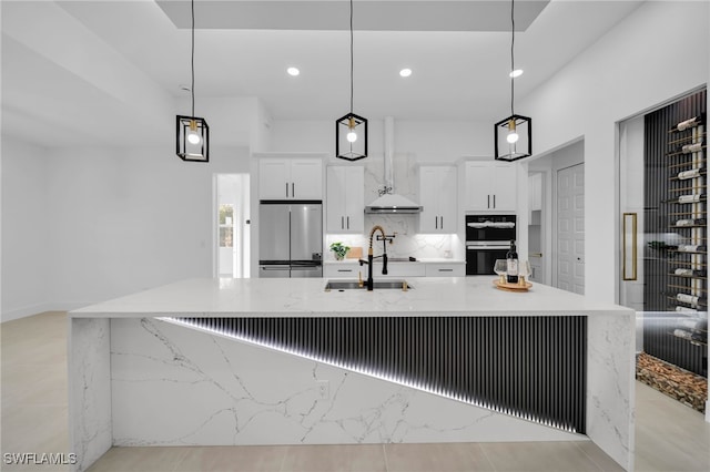 kitchen featuring a spacious island, a sink, stainless steel refrigerator, white cabinetry, and multiple ovens