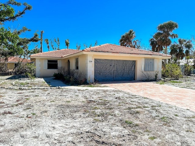 ranch-style home featuring a tiled roof, a garage, driveway, and stucco siding