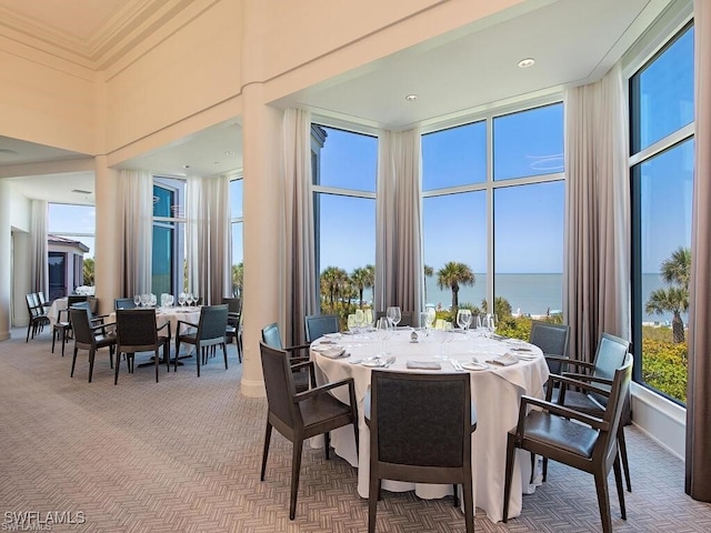 carpeted dining area featuring a towering ceiling and a water view