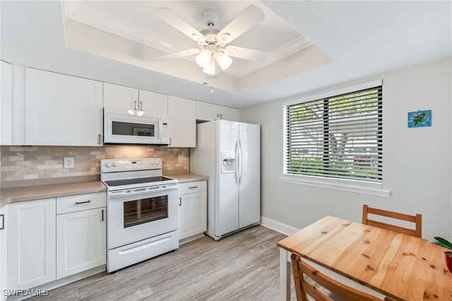 kitchen featuring light countertops, a tray ceiling, decorative backsplash, white appliances, and white cabinetry