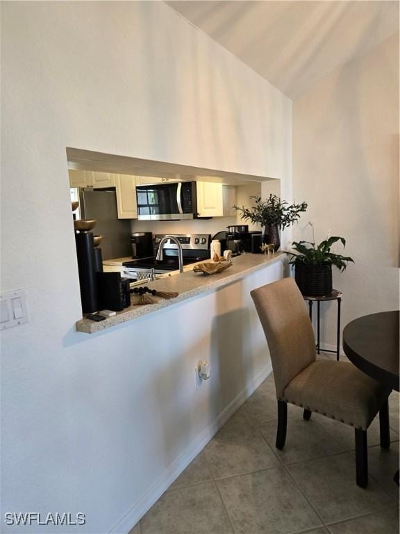 kitchen featuring tile patterned floors, high vaulted ceiling, a sink, appliances with stainless steel finishes, and light countertops