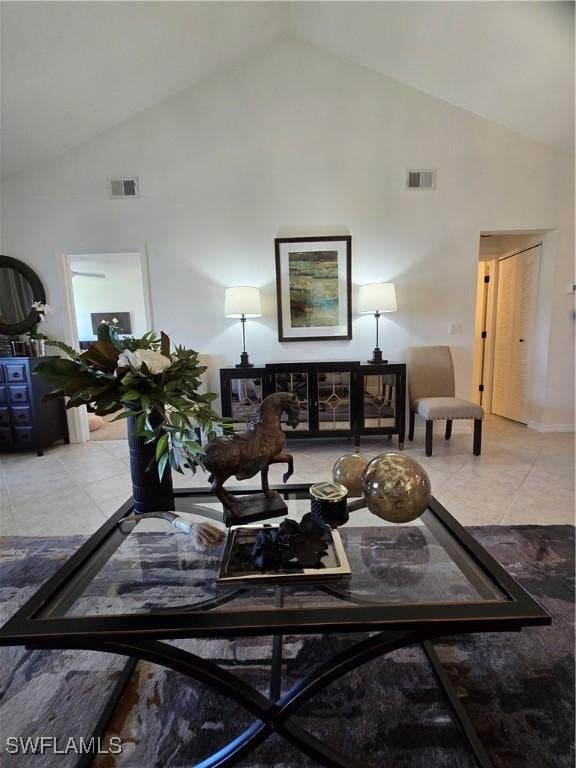 living area with tile patterned floors, visible vents, and high vaulted ceiling