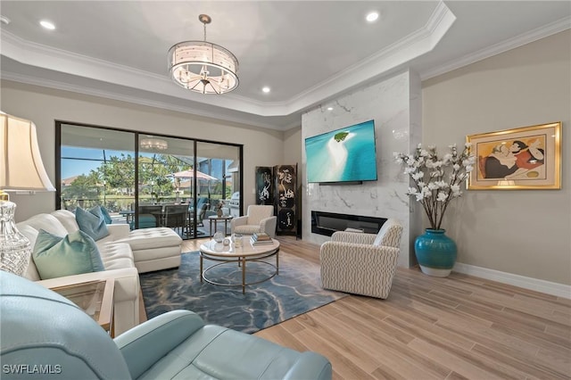 living room with crown molding, a fireplace, a raised ceiling, and wood finished floors