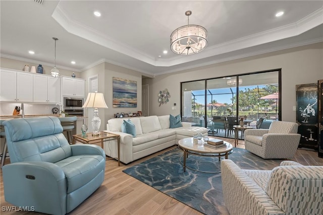 living room featuring a notable chandelier, a raised ceiling, light wood-style floors, and ornamental molding