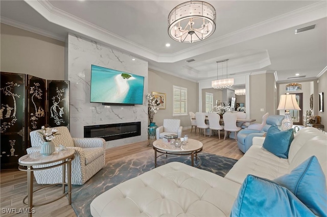 living area with wood finished floors, visible vents, a premium fireplace, a tray ceiling, and a notable chandelier