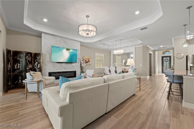 living room featuring visible vents, a notable chandelier, light wood finished floors, a premium fireplace, and a raised ceiling