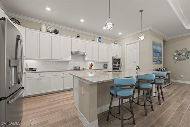 kitchen with ornamental molding, white cabinets, under cabinet range hood, appliances with stainless steel finishes, and light wood-type flooring