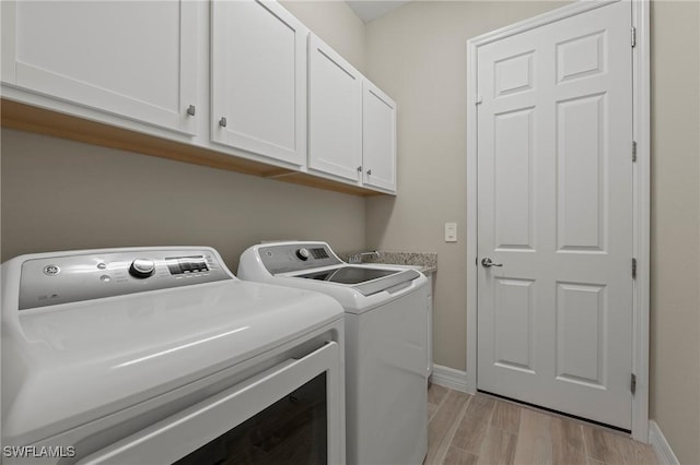 clothes washing area with baseboards, cabinet space, light wood-type flooring, and washing machine and clothes dryer