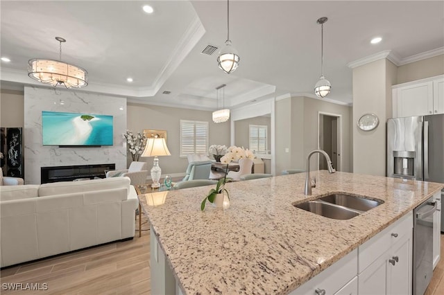 kitchen featuring a kitchen island with sink, a sink, open floor plan, white cabinetry, and light wood-style floors