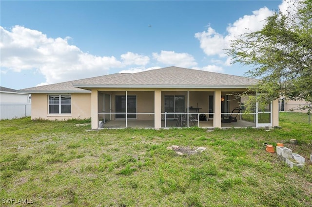 rear view of house with stucco siding, a lawn, fence, roof with shingles, and a sunroom