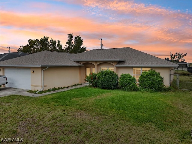 ranch-style home with fence, roof with shingles, an attached garage, stucco siding, and a lawn