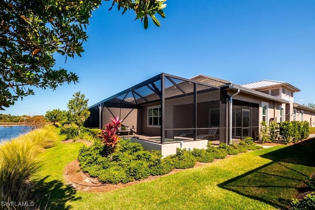 rear view of house with stucco siding, a water view, a lanai, a lawn, and metal roof