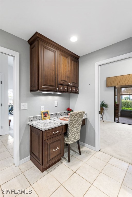 kitchen featuring light tile patterned floors, baseboards, dark brown cabinets, and built in desk