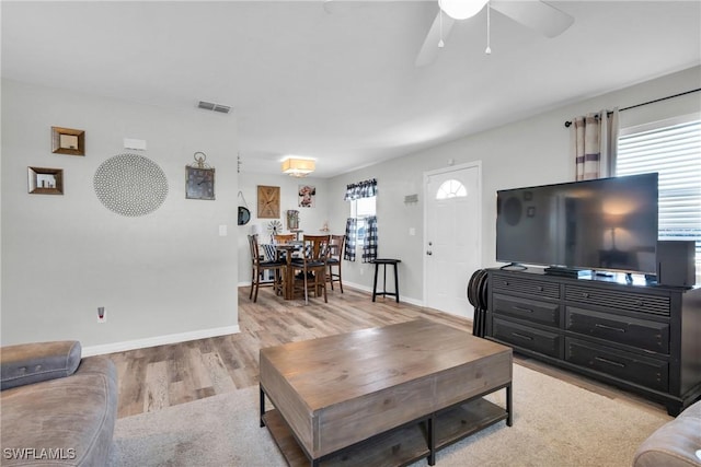 living area with visible vents, light wood-style flooring, baseboards, and ceiling fan