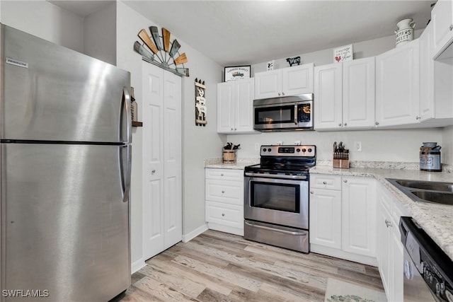 kitchen with light stone countertops, a sink, light wood-style floors, appliances with stainless steel finishes, and white cabinetry