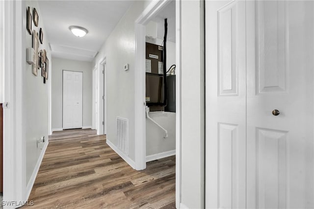 hall with visible vents, baseboards, and wood finished floors