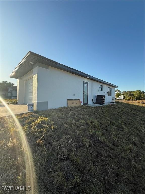 rear view of house featuring cooling unit, an attached garage, and stucco siding