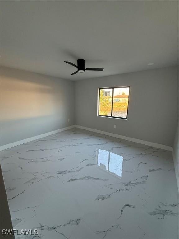 empty room with marble finish floor, baseboards, and ceiling fan