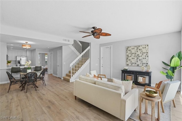 living area featuring visible vents, stairway, light wood-style floors, baseboards, and ceiling fan