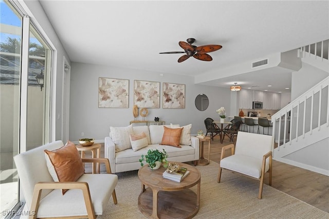 living area featuring light wood finished floors, visible vents, baseboards, stairway, and a ceiling fan