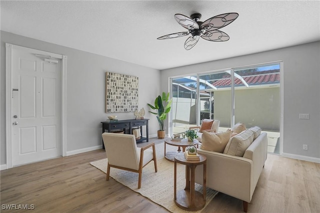 living area featuring baseboards, light wood finished floors, and ceiling fan