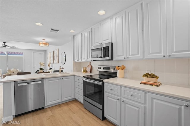 kitchen featuring visible vents, a sink, stainless steel appliances, a peninsula, and white cabinets