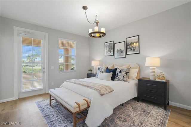 bedroom with access to exterior, a chandelier, baseboards, and wood finished floors