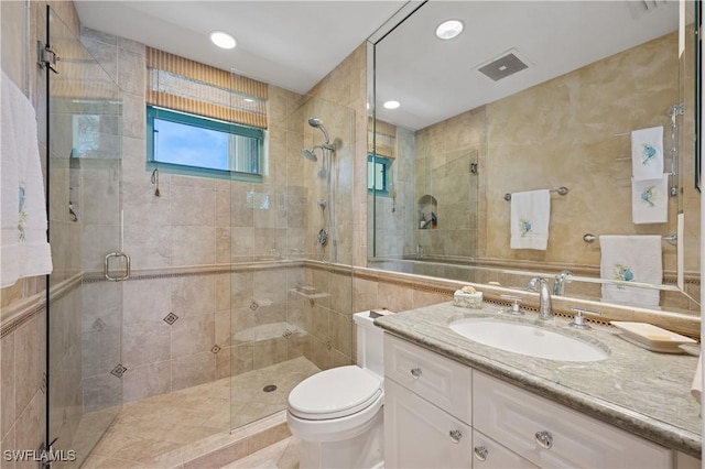 full bath with vanity, visible vents, a shower stall, tile walls, and toilet