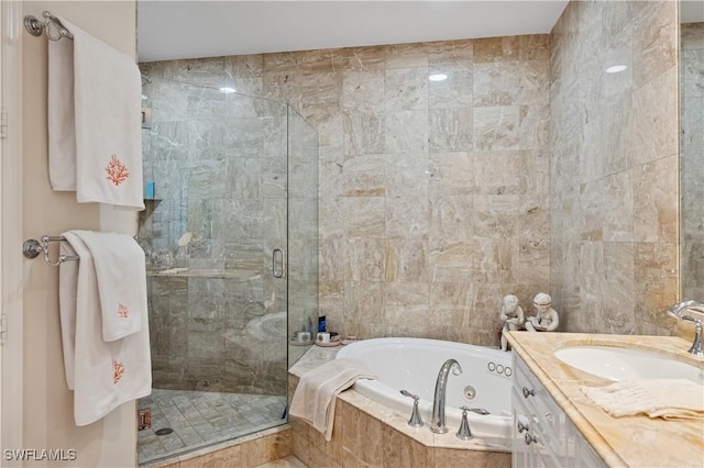 bathroom with tile walls, a stall shower, a jetted tub, and vanity