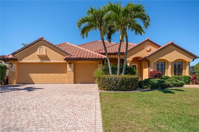 mediterranean / spanish house featuring a front lawn, a tiled roof, stucco siding, decorative driveway, and an attached garage