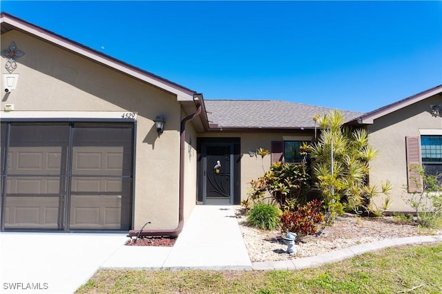 property entrance with stucco siding, a garage, and roof with shingles