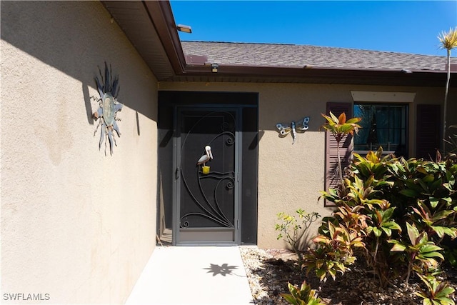 view of exterior entry featuring roof with shingles and stucco siding