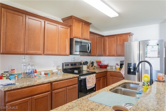 kitchen with light stone counters, brown cabinets, appliances with stainless steel finishes, and a sink