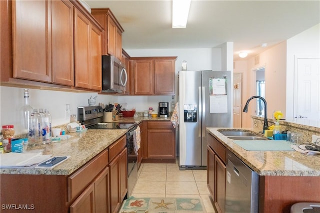 kitchen featuring light stone counters, light tile patterned floors, a sink, stainless steel appliances, and brown cabinets