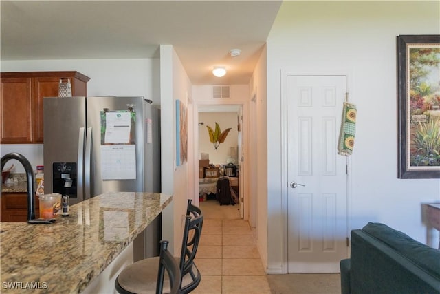 kitchen with light stone counters, light tile patterned floors, visible vents, stainless steel refrigerator with ice dispenser, and brown cabinets